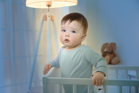 Cute little baby standing in crib at homeの写真素材