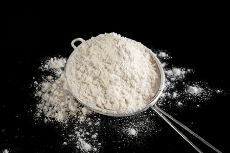 Sieve with flour on black background