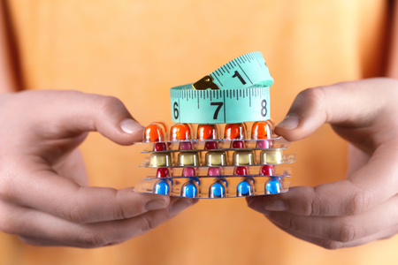 Young woman holding packs of pills and measuring tape in hands, closeup. Weight loss conceptの写真素材