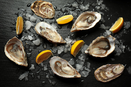 Delicious oysters with slices of lemon and ice cubes on dark tableの写真素材