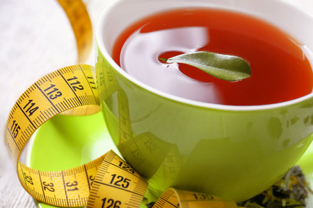 Closeup view of cup with tea, leaf and measuring tape on table. Weight loss conceptの写真素材