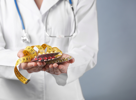 Doctor holding packs of pills and measuring tape in hands, closeup. Weight loss conceptの写真素材