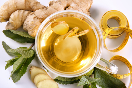 Composition with cup of tea, ginger, mint leaves and measuring tape on white background. Weight loss...