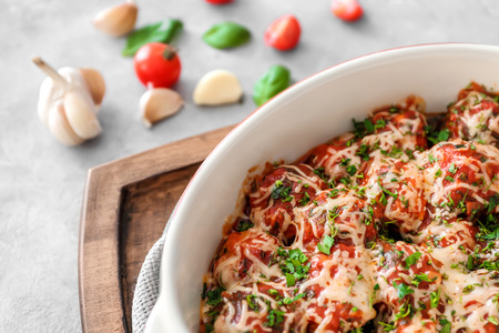 Ceramic casserole dish with turkey meatballs, tomato sauce and melted cheese on tableの写真素材