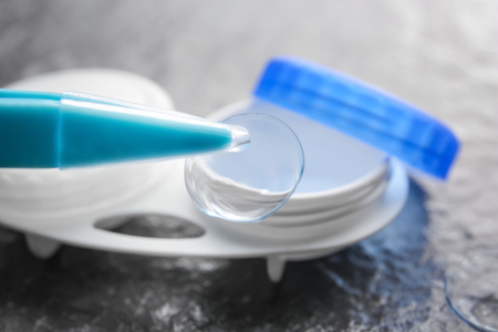 Tweezers with contact lens and blurred container on gray textured backgroundの写真素材