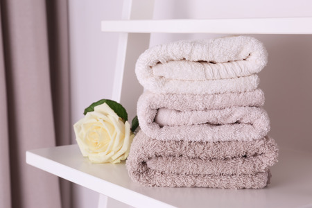 Stack of clean towels and beautiful rose on shelfの写真素材