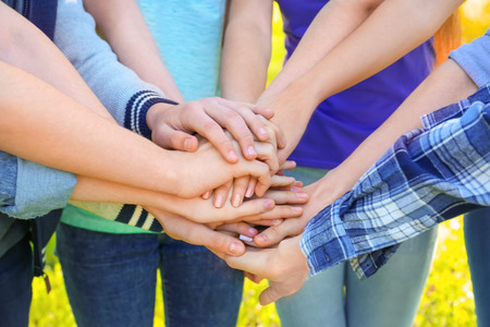 Young people putting hands together outdoors. Volunteer concept