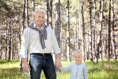 Happy senior man with granddaughter in forest on sunny dayの写真素材