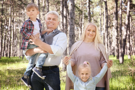 Happy grandparents and children in forest on sunny day