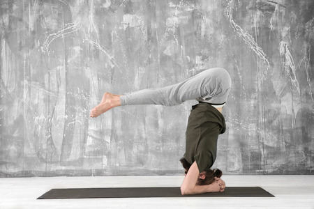 Young man practicing yoga on gray wall background