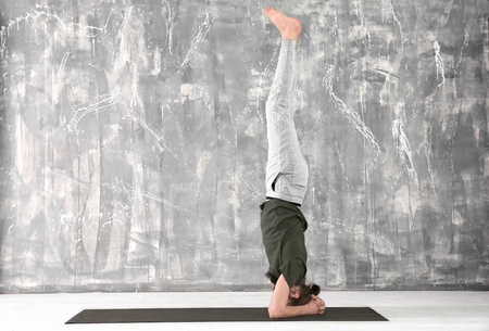 Young man practicing yoga on gray wall background