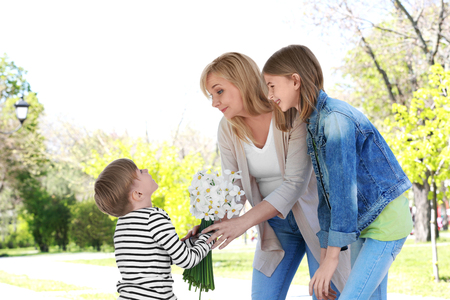 Cute little boy giving bouquet of flowers to his grandmother in spring park on sunny dayの写真素材