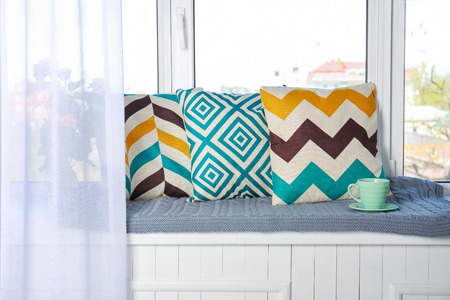 Stylish pillows and plaid with cup of tea on window sillの写真素材