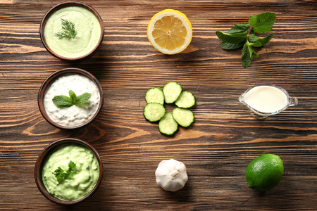 Delicious yogurt sauces in bowls with ingredients on wooden tableの写真素材