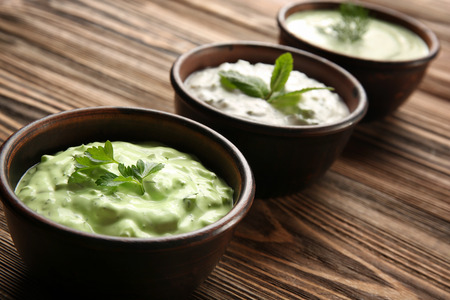 Delicious yogurt sauces in bowls on wooden background