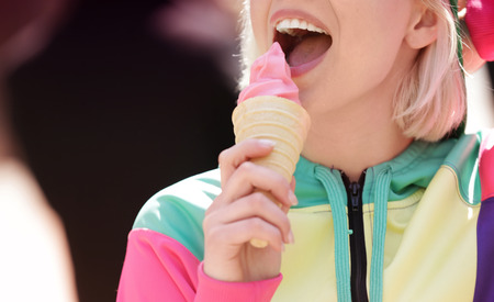 Beautiful young girl eating tasty yogurt ice cream on blurred background, closeup