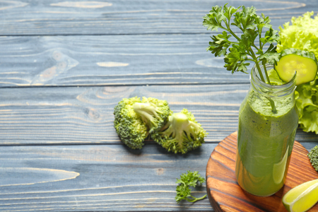 Glass bottle with fresh green juice and ingredients on tableの写真素材