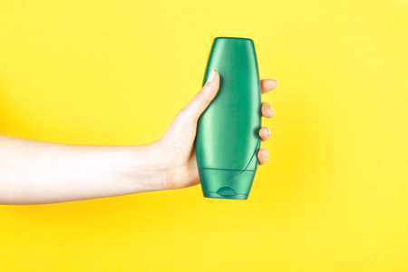 Female hand with bottle of cosmetic product for shower on color background