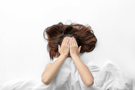 Young woman lying in bed and covering face with hands