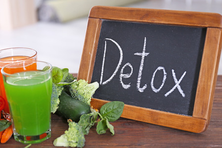 Small chalkboard with word DETOX, fresh juices in glasses and ingredients on tableの写真素材