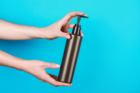 Female hands with bottle of cosmetic product for shower on color backgroundの写真素材