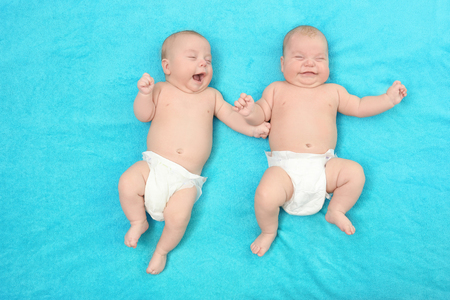 Beautiful baby twins lying together on blue textile backgroundの写真素材