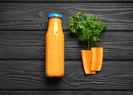 Bottle of fresh smoothie, carrot slices and parsley on wooden backgroundの写真素材