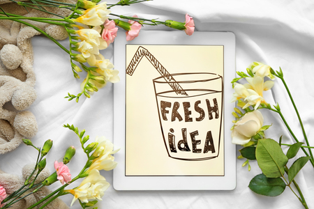 Beautiful composition with tablet computer and fresh flowers on fabric backgroundの写真素材