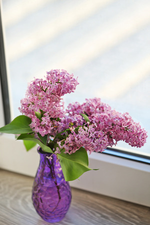 Glass vase with beautiful lilac flowers on window sillの写真素材