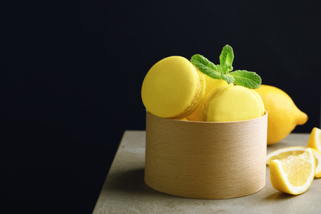 Box with tasty lemon macarons on table against dark backgroundの写真素材