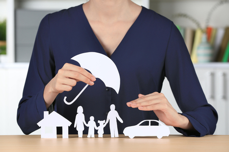 Woman holding umbrella over paper silhouette of family, house and car on table. Insurance conceptの写真素材