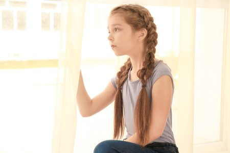 Sad little girl near window at homeの写真素材