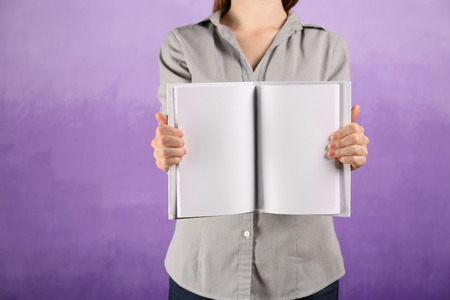 Woman holding open book with blank pages on color background