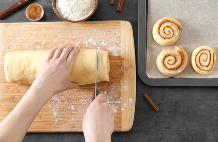 Woman cutting dough for cinnamon rolls on wooden boardの写真素材