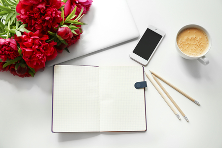Open notebook and beautiful fragrant peonies on light tableの写真素材