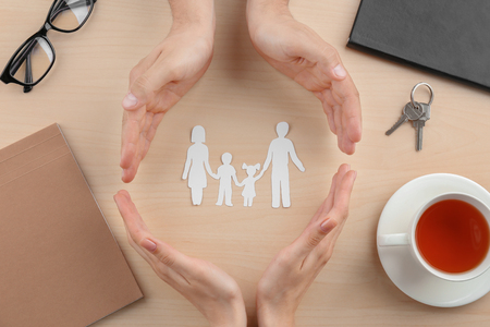 Hands making circle and protecting paper silhouette of family on table. Insurance conceptの写真素材