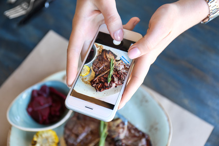 Woman hands with mobile phone photographing tasty beefsteak, closeupの写真素材