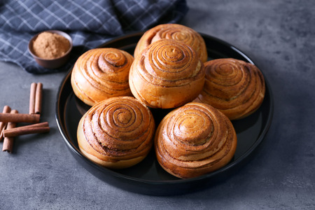 Black round plate with yummy cinnamon rolls on kitchen tableの写真素材