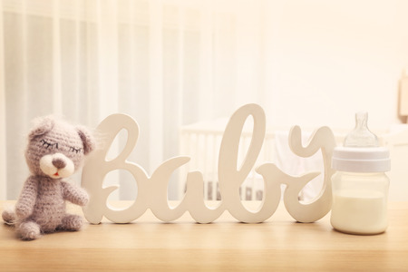 Handmade knitted baby toy with decor and bottle of milk on table in bedroomの写真素材