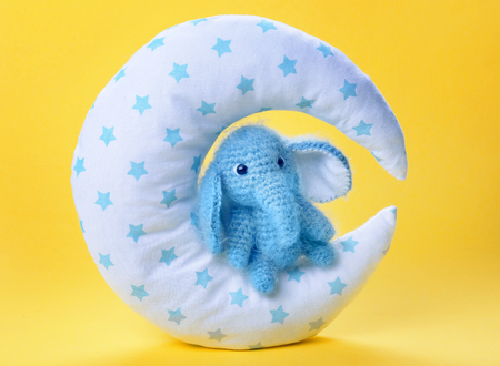 Cute handmade elephant toy with pillow in shape of moon on color background, closeupの写真素材