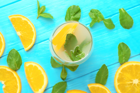 Glass of fresh orange lemonade on color background