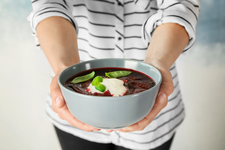 Woman holding bowl with beet soup on light backgroundの写真素材