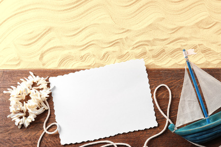 Composition with wooden board, blank card, coral necklace and small ship on sand. Concept of travel and vacationの写真素材
