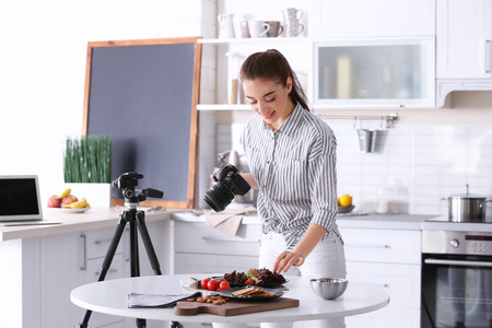 Young woman with professional camera taking still life pictures in kitchenの写真素材