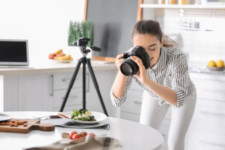 Young woman with professional camera taking still life pictures in kitchenの写真素材