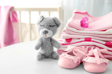Knitted toy bear and baby clothes on tableの写真素材