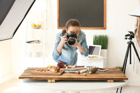 Young woman with professional camera taking still life pictures in photo studioの写真素材