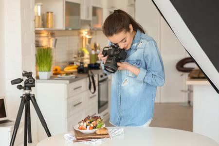 Young woman with professional camera taking still life pictures in kitchenの写真素材