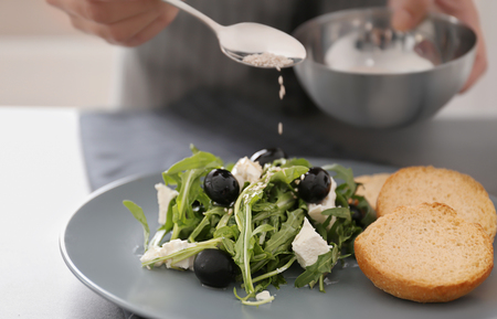 Woman dressing fresh vegetable salad with arugula leaves and olivesの写真素材