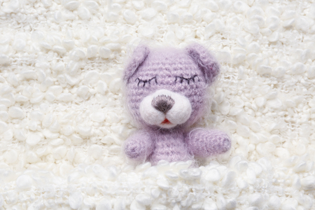 Cute knitted bear on white fluffy fabric backgroundの写真素材